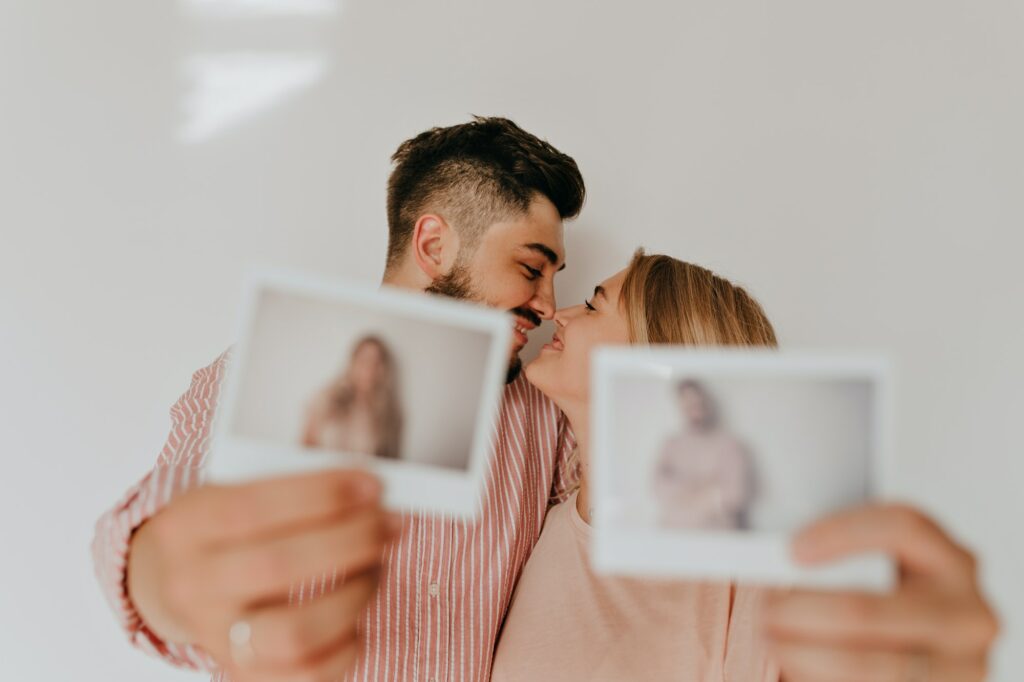 Husband and wife in love looking tenderly at each other and smile, holding their Polaroid portraits
